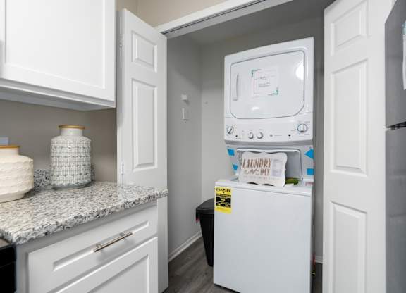 A kitchen with granite countertops, white cabinets, and a washer and dryer unit at Summerchase at Riverchase in Hoover, Alabama.