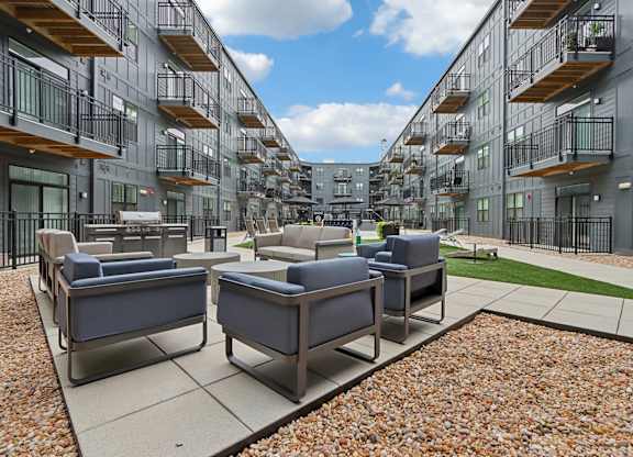 A patio with couches and chairs is surrounded by apartment buildings.