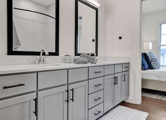 Modern bathroom with double vanity, gray cabinets, quartz countertops, and designer plank flooring at West Row Lofts and Townhomes in Birmingham, AL.