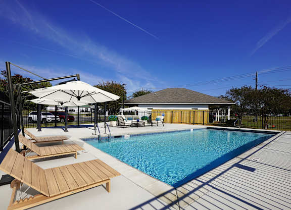 A pool with sun loungers and a white umbrella.