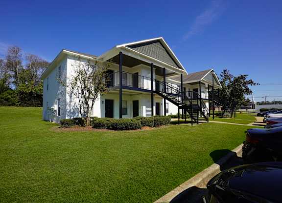 A white house with a black balcony is surrounded by green grass.