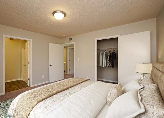 A bedroom with a large bed and a closet with clothes hanging.