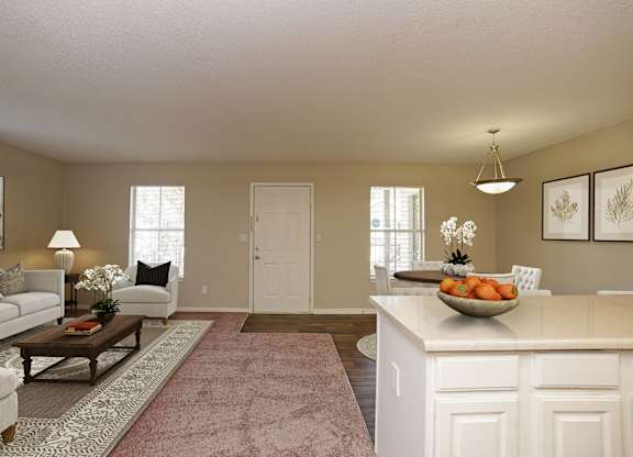 A well-lit, spacious living room with a white sofa, a coffee table, and a large kitchen island.