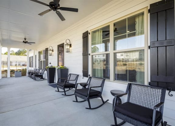 the front porch of a house with rocking chairs and a ceiling fan