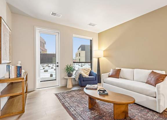 A living room with a white couch, a wooden coffee table, and a large window with a view of the outside.