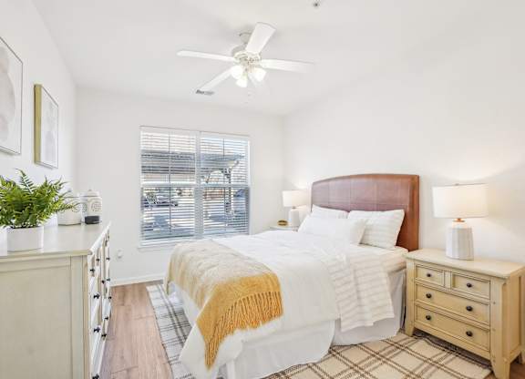 A bedroom with a bed, nightstand, and a plant on the windowsill.