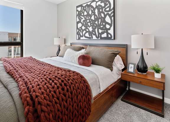a bedroom with a bed and a table with lamps and a window
