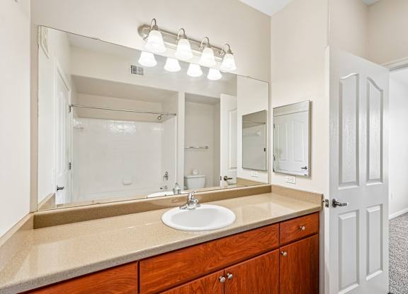 A bathroom with a sink, mirror, and lighting fixture.