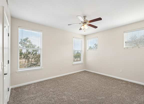 A room with a ceiling fan and two windows.
