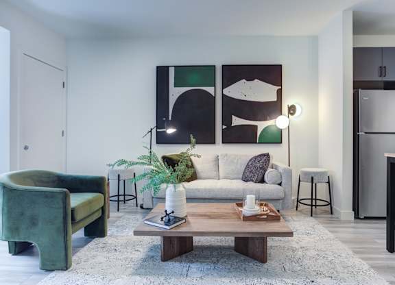 A living room with a green chair, a white couch, and a painting on the wall.