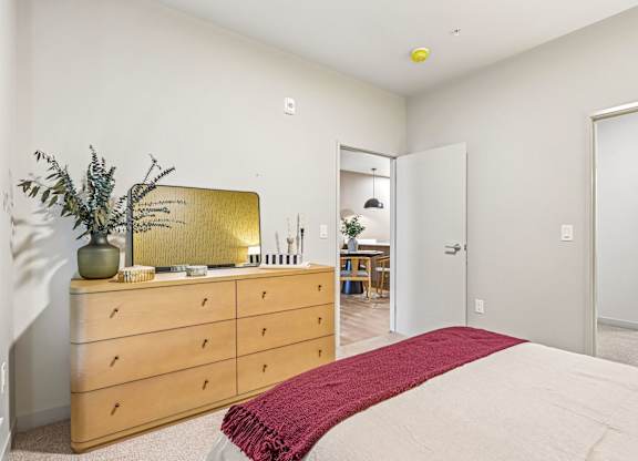 A bedroom with a bed, dresser, mirror, and a plant.