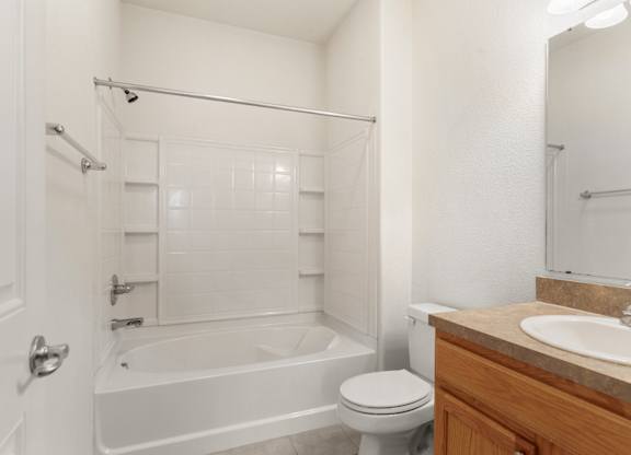 5-Bedroom Apartments in Lawrence, KS - Ironwood Apartments and Townhomes - Bathroom with Ceramic Tile Surround Bathtub, Single-Sink Vanity, Large Mirror, and Light Fixtures