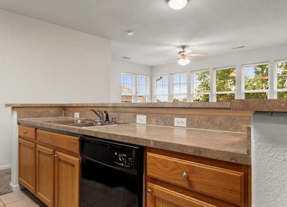 A kitchen with a black dishwasher and wooden cabinets.