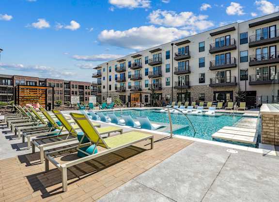 A sunny day at the poolside with lounge chairs and apartment buildings in the background.