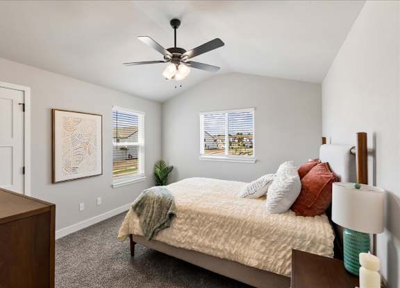 A bedroom with a bed, a ceiling fan, and a painting on the wall.