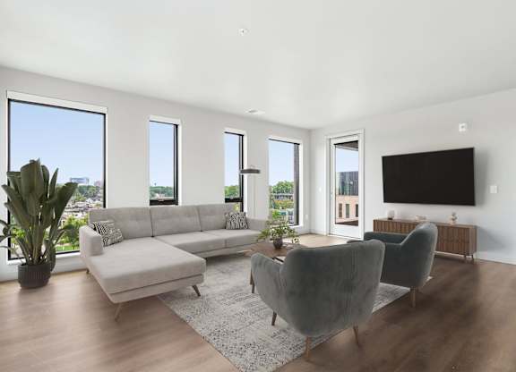 A living room with a grey couch, a grey chair, a grey ottoman, a television, and a potted plant.