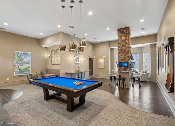 A pool table is in the middle of a room with a wood floor and a stone pillar.