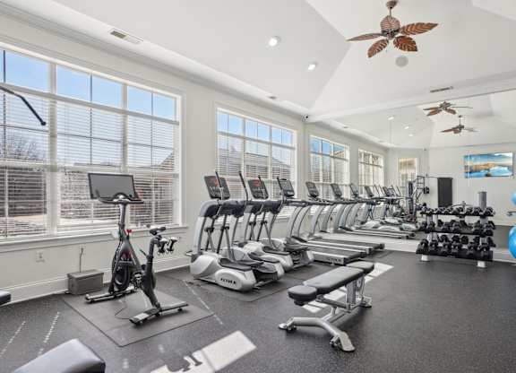 A spacious gym with a variety of exercise equipment and a ceiling fan.