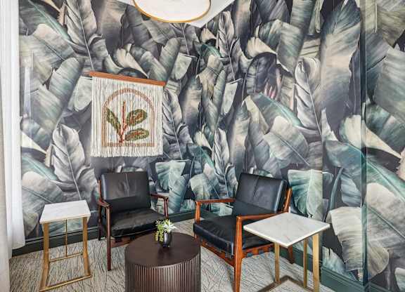 A living room with a banana leaf wallpaper and a round table with a vase on it.