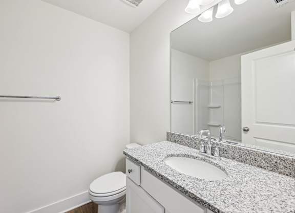 A bathroom with a toilet, sink, mirror, and towel rack.