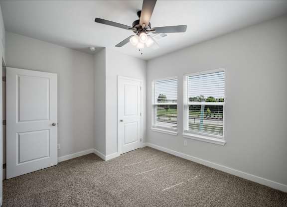 A room with a ceiling fan and two windows.