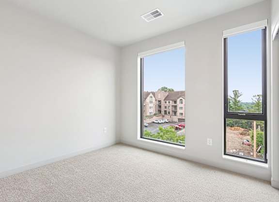 A large empty room with a view of a building and trees outside the window.