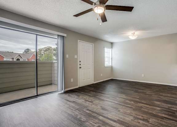 an empty living room with a sliding glass door and a ceiling fan