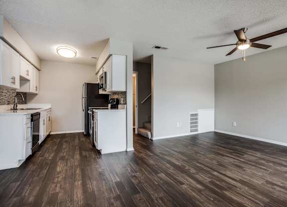 an empty living room with a kitchen and a ceiling fan