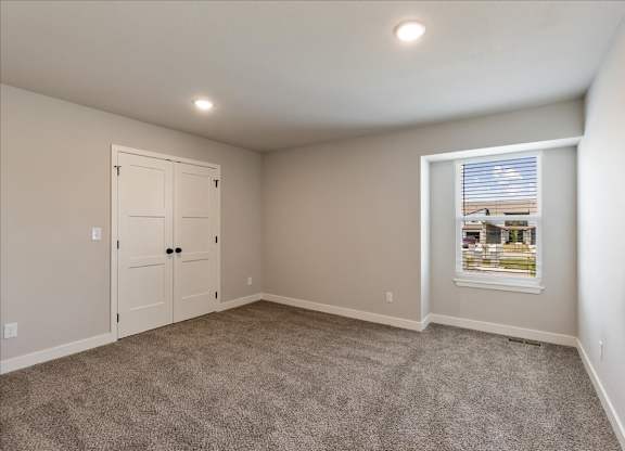A room with a carpeted floor, a white door, and a window with blinds.
