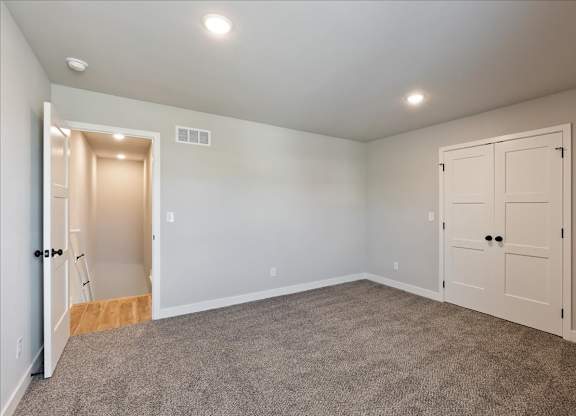 A room with a carpeted floor and two doors, one of which is open.