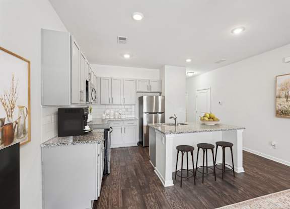 A kitchen with white cabinets and a white island with three stools.