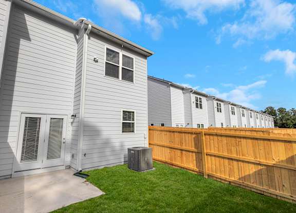 A grey house with a brown fence and a green lawn.
