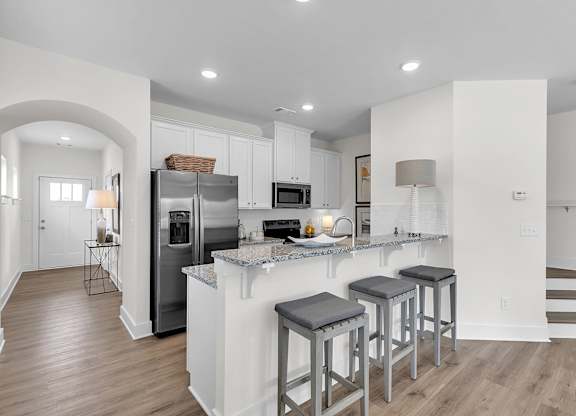 A kitchen with a refrigerator, stove, and bar stools.