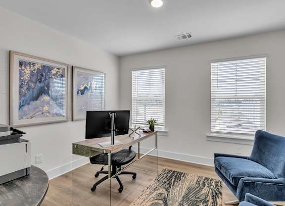 A room with a desk, chair, and two framed pictures on the wall.