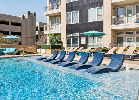 A row of blue lounge chairs are arranged around a swimming pool.