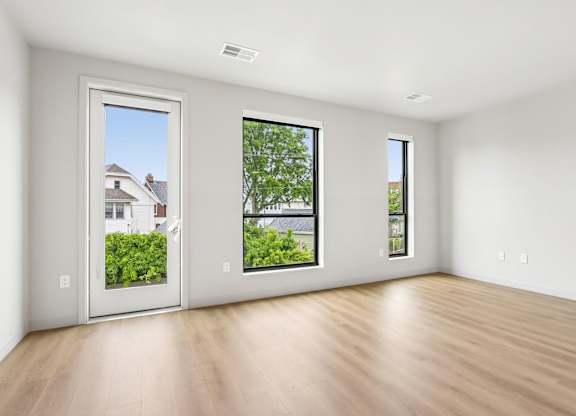 A room with a wooden floor and three windows showing the outdoors.