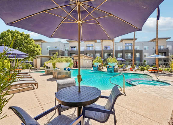 A purple umbrella is over a table with chairs and a pool in the background.