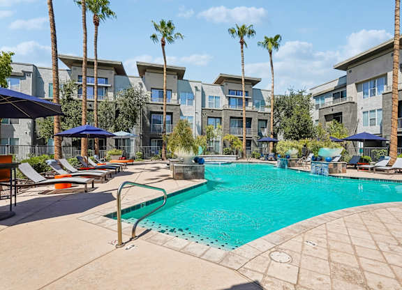 A swimming pool surrounded by palm trees and lounge chairs.