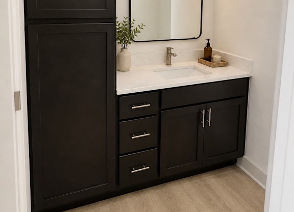 A bathroom with a sink, mirror, and black cabinetry.