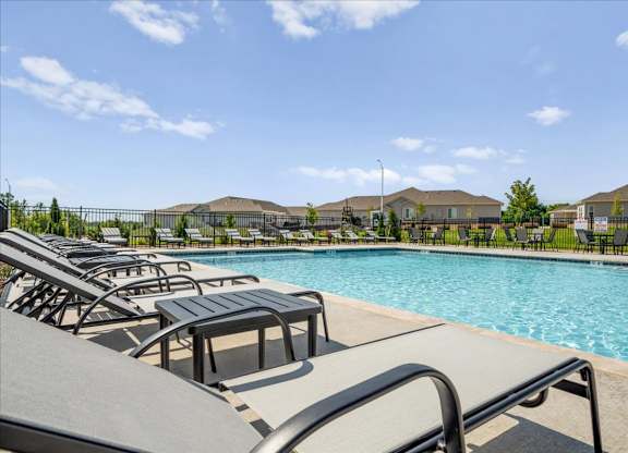 A pool with sun loungers and a fence in the background.