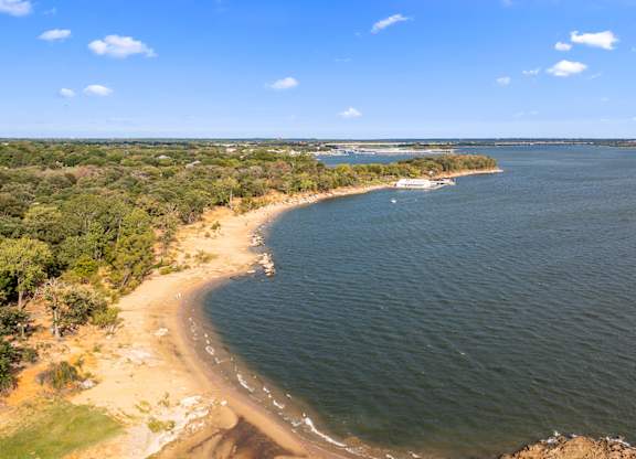 A beach with a boat in the water and trees on the land.