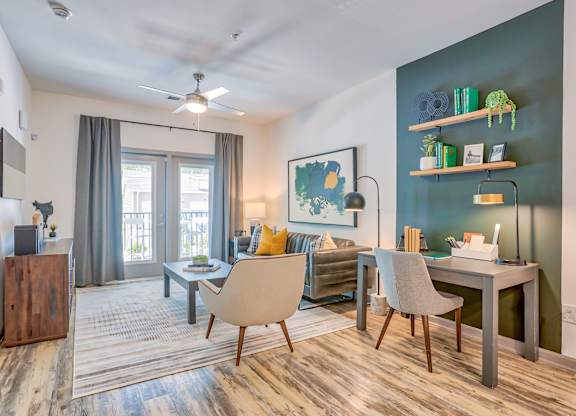 A room with a desk, chairs, and a ceiling fan.