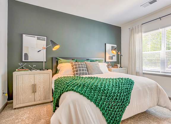 A bedroom with a white bed and a green knitted blanket.