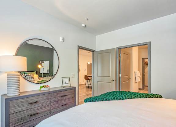 A bedroom with a bed, dresser, mirror, and a green pillow.