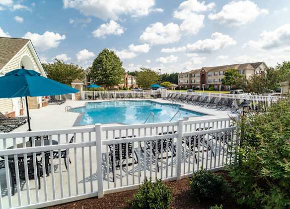 A pool surrounded by a white fence with chairs and umbrellas.