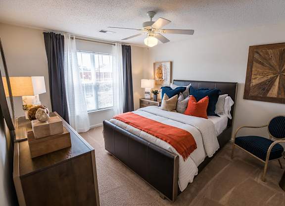 A bedroom with a bed, chair, and a ceiling fan.
