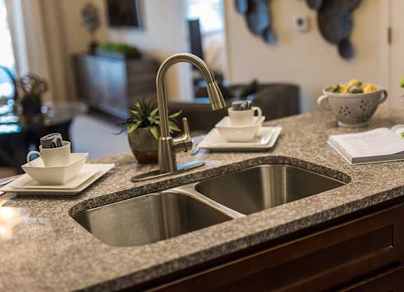 A kitchen sink with a silver faucet and a plant on the counter.