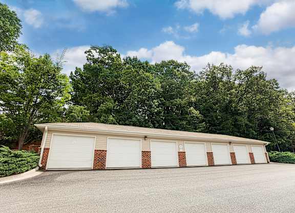 A two-car garage with a brick facade is surrounded by a gravel driveway and lush green trees.