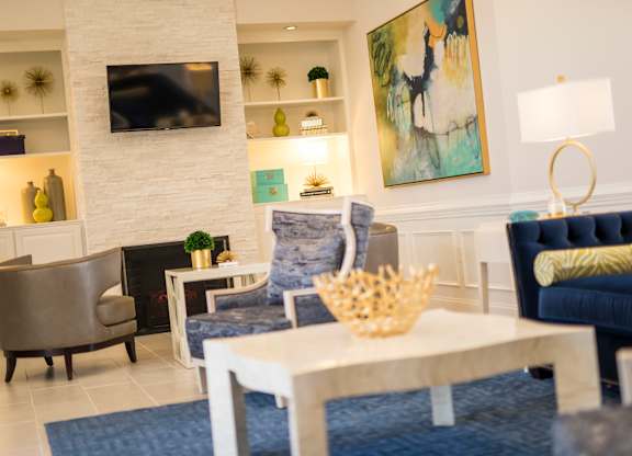 A living room with a grey chair, a white table, a blue couch, and a painting on the wall.