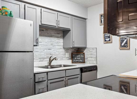 A kitchen with a refrigerator, sink, and cabinets.